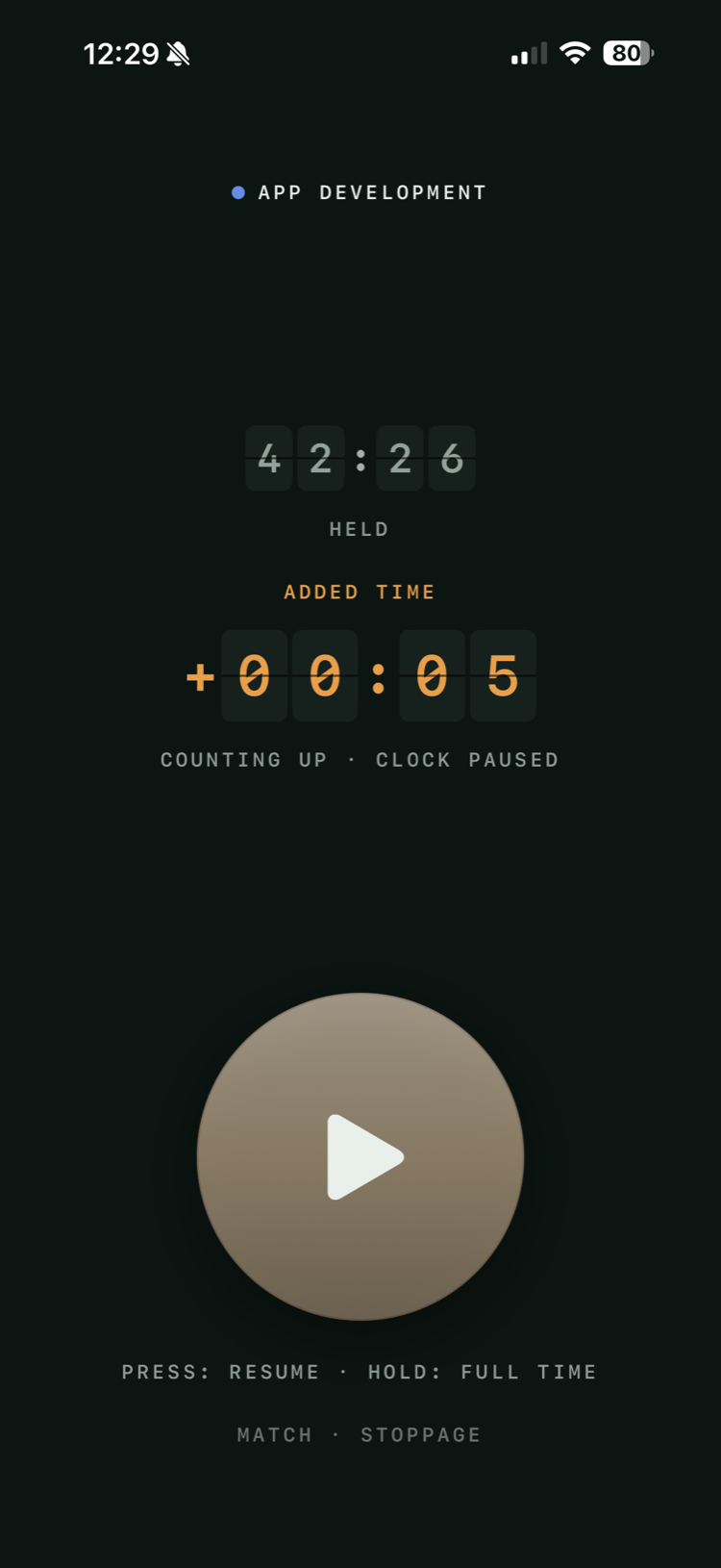 The same screen held: the clock greyed at 42:26 under the word HELD, and beneath it “ADDED TIME” with +00:05 counting up in orange split-flap digits, labelled counting up · clock paused. The disc has dimmed to a play symbol.